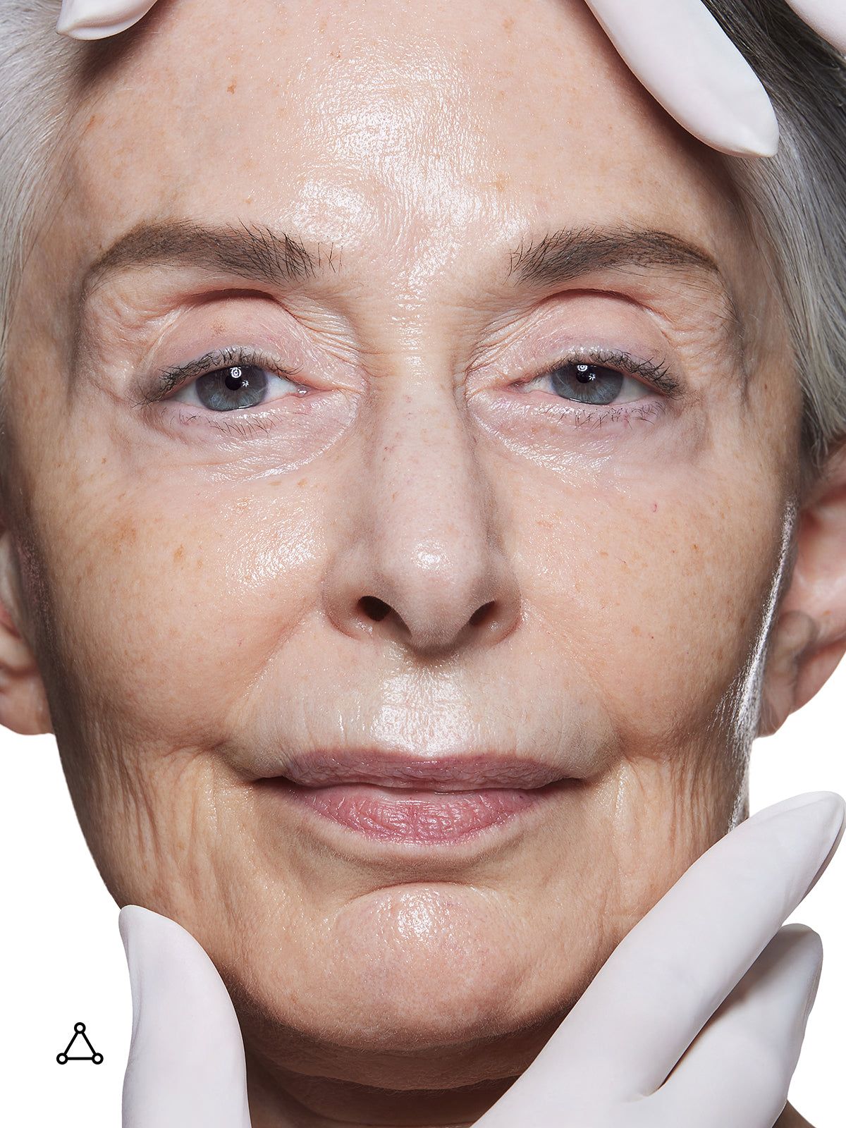 Portret van een oudere vrouw. Handen met handschoenen raken haar gezicht aan. Huidverzorgingscontext.