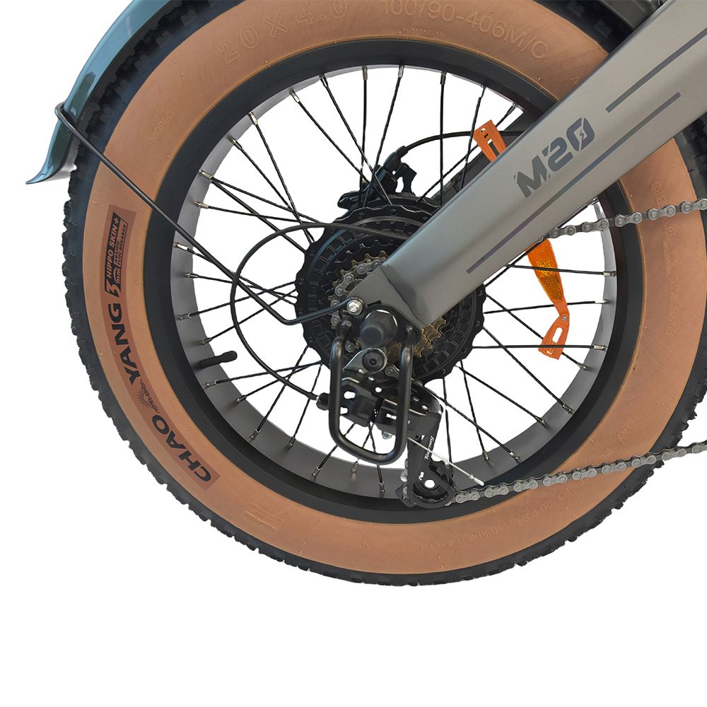 Gros plan de la roue arrière d'un dirt bike électrique gris. Pneu marron, chaîne noire et détails. Inscription 'M20'.