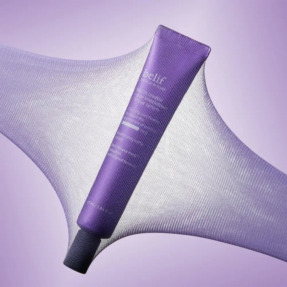 Tube de crème pour les yeux Belif sur tissu violet. Le tissu est extensible et transparent.