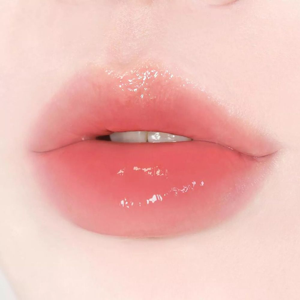 Gros plan sur des lèvres avec un baume teinté rose brillant. Les lèvres sont légèrement entrouvertes.