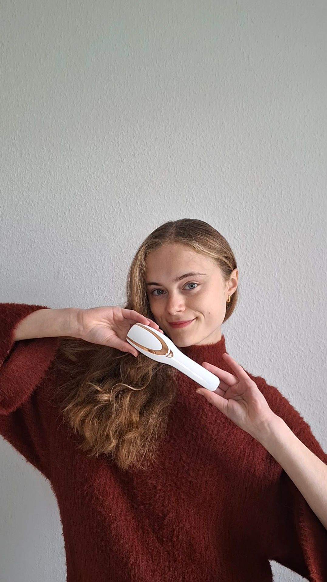 Appareil de brosse à cheveux blanc et doré. Une femme tient l'appareil devant ses cheveux. L'appareil est de forme ovale.