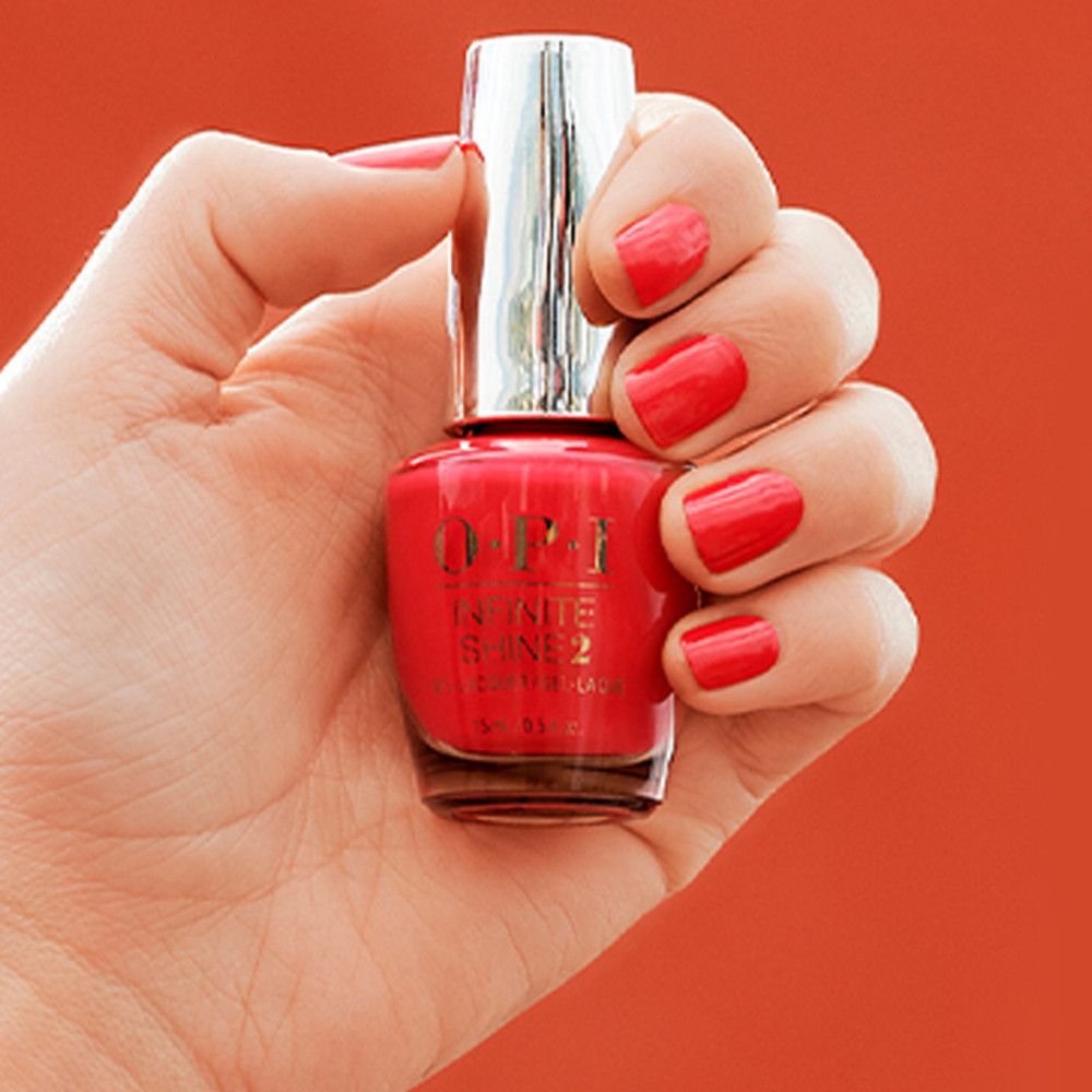 Flacon de vernis à ongles rouge. Bouchon argenté. Main avec ongles vernis tenant le flacon sur fond rouge.