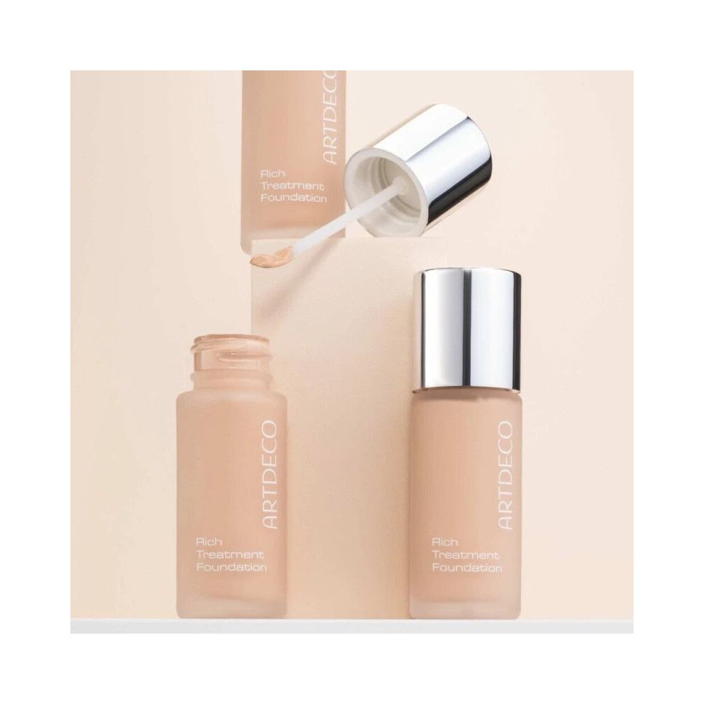 Artdeco Rich Treatment Foundation. Flacon avec bouchon argenté et applicateur. Flacon ouvert et produit à côté.