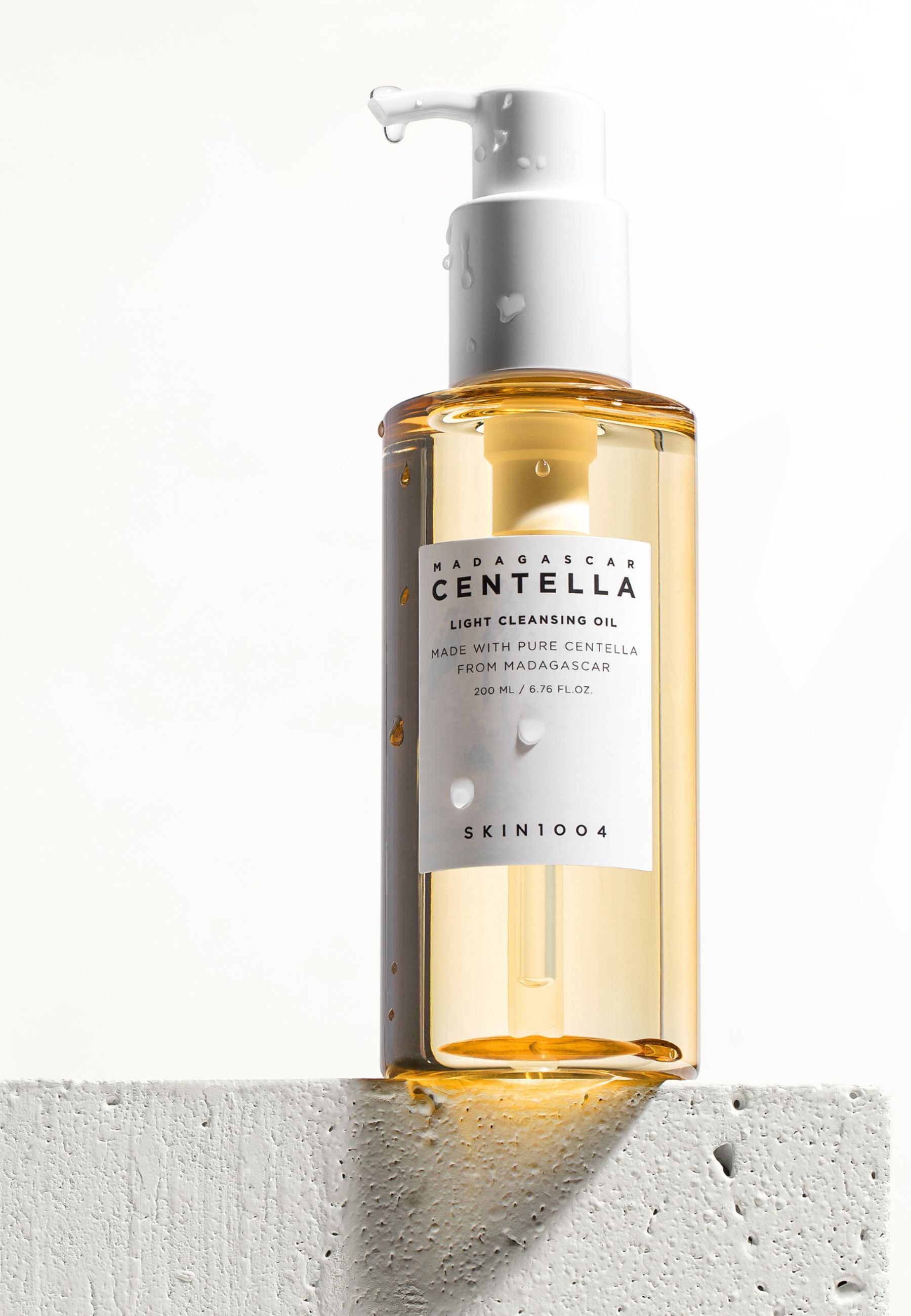 Flacon transparent avec pompe blanche. Étiquette : MADAGASCAR CENTELLA, LIGHT CLEANSING OIL, SKIN1004. Gouttes d'eau.