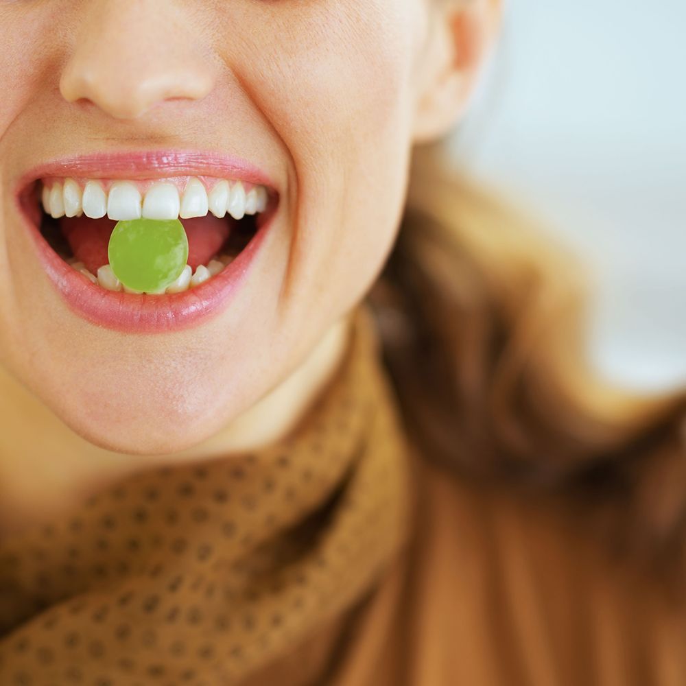 Close-up van persoon die groene gummy in mond neemt.