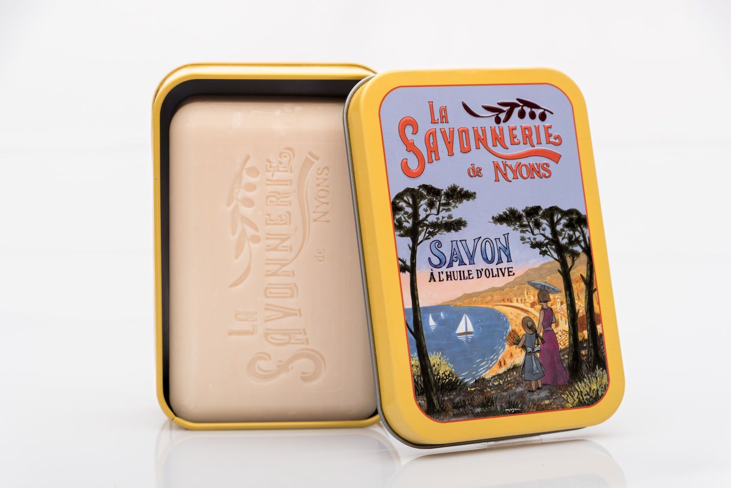 Boîte métallique jaune ouverte avec savon. Sur le couvercle : "La Savonnerie de Nyons" et paysage. Savon estampillé.