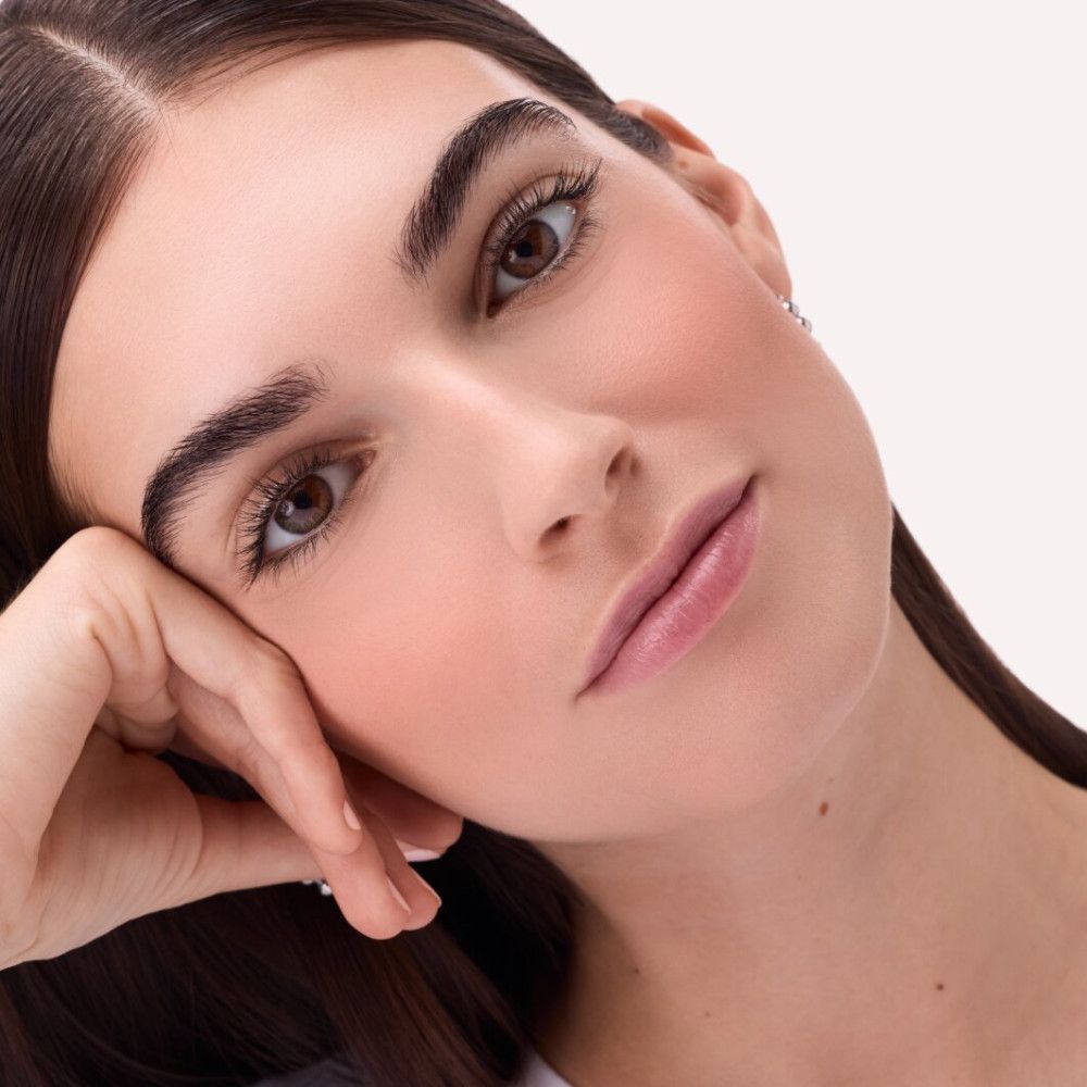 Portrait d'une femme avec du blush sur les joues. Elle soutient son menton avec sa main.