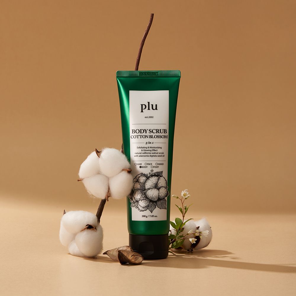 Tube vert avec étiquette blanche. Inscription : PLU, BODY SCRUB COTTON BLOSSOM. Illustration : fleurs de coton. Branches et fleurs de coton.