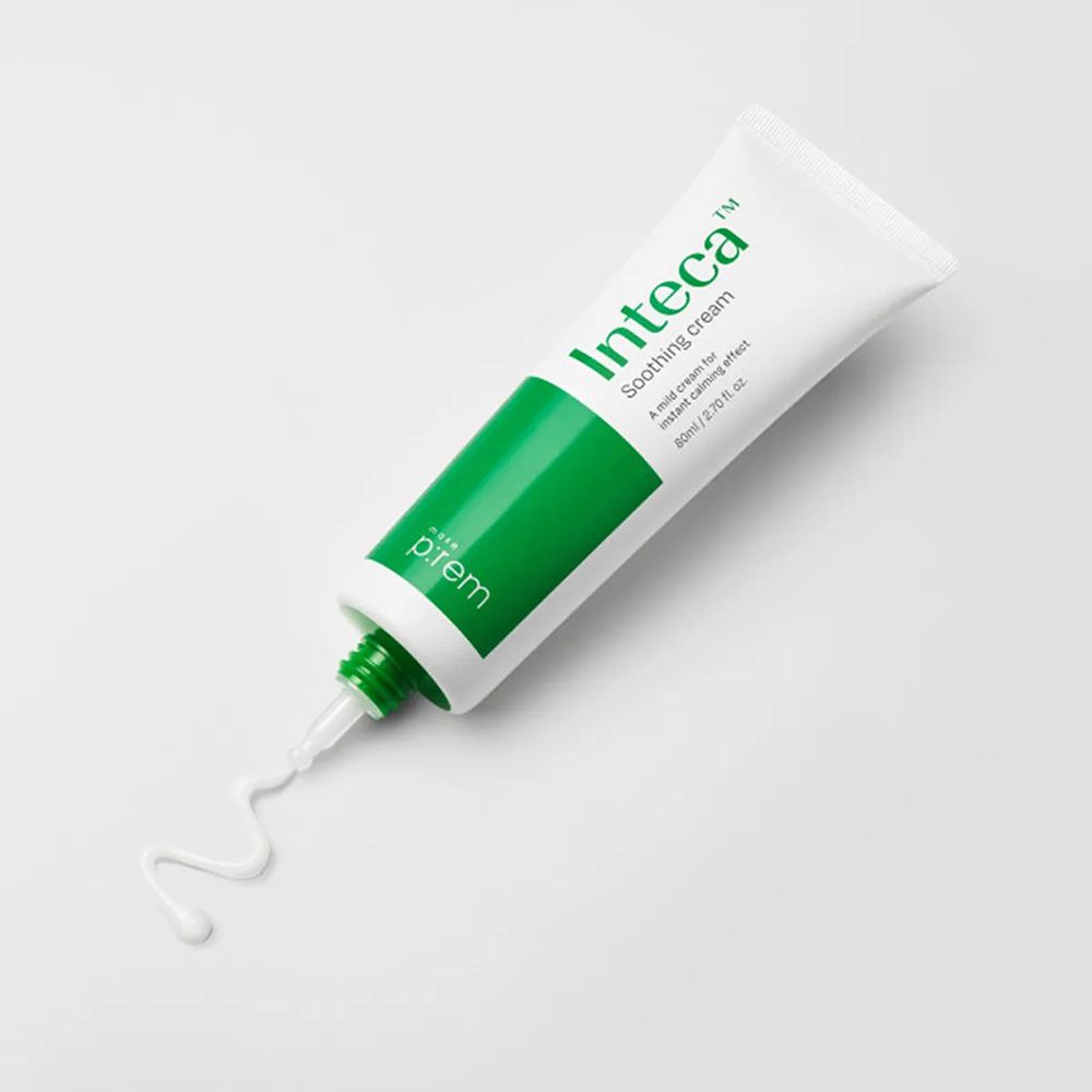 Witte tube met groene streep en tekst 'Inteca Soothing cream'. Crème komt eruit.