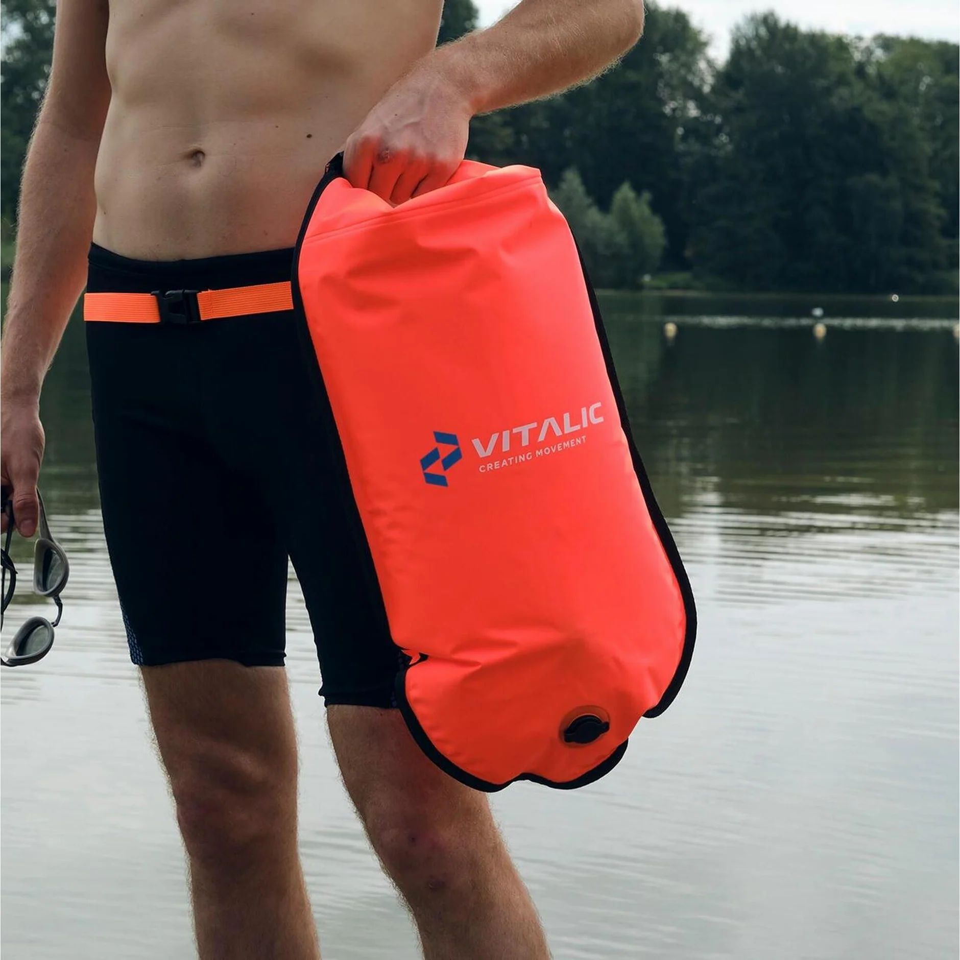 Personne tenant une bouée orange au bord du lac. La personne porte un maillot de bain et des lunettes de soleil.
