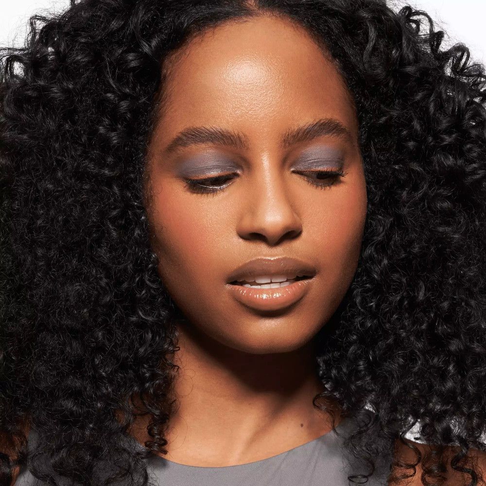 Portrait d'une femme aux cheveux bouclés. Elle porte de l'ombre à paupières et du rouge à lèvres.