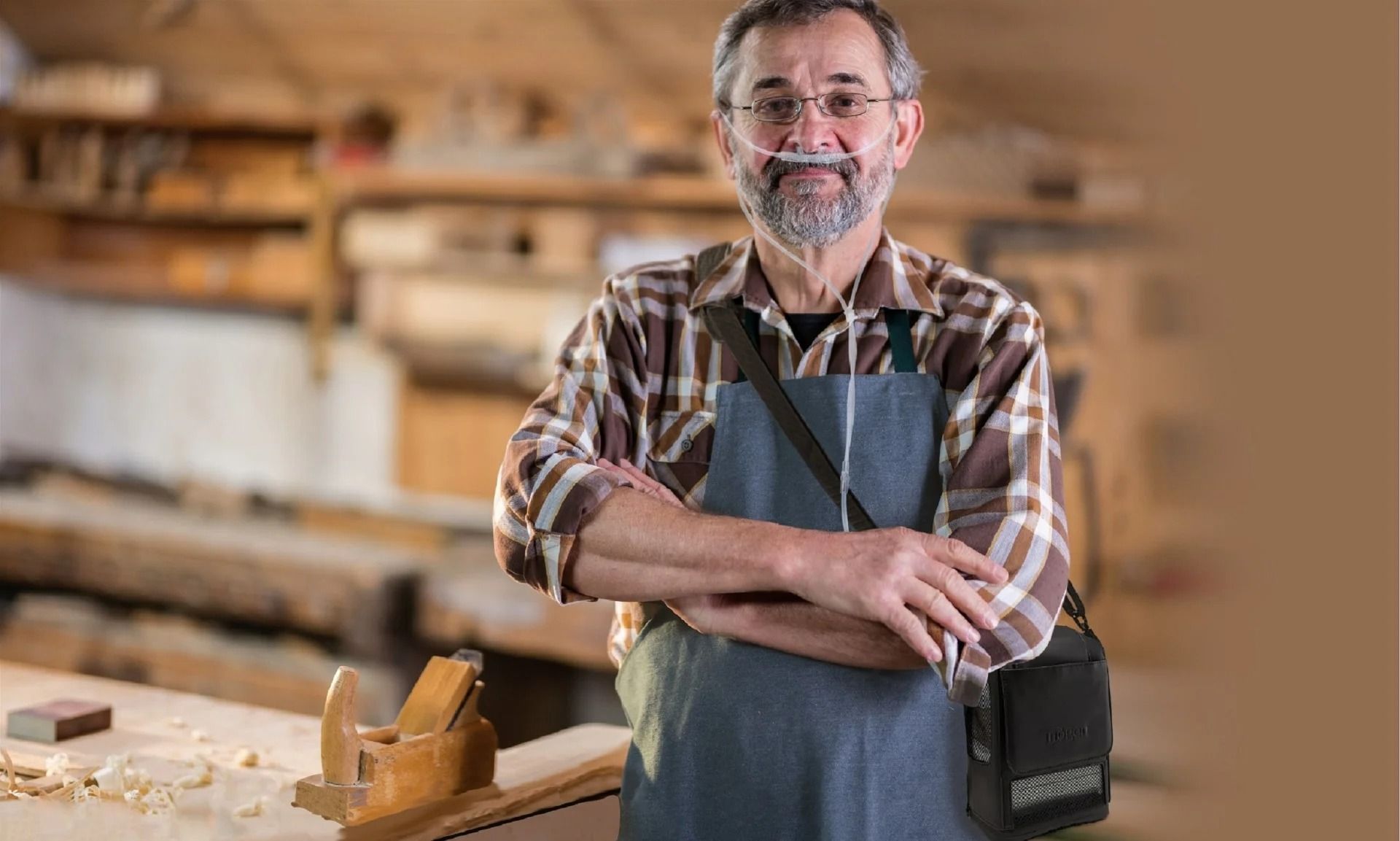 Man met neusbril en mobiele zuurstofconcentrator in een werkplaats.