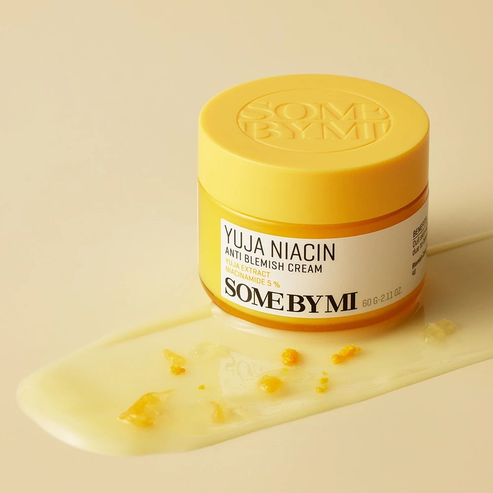 Pot de crème jaune avec couvercle et étiquette blanche. Inscription: YUJA NIACIN, ANTI BLEMISH CREAM, SOME BY MI. Tache de crème à côté.