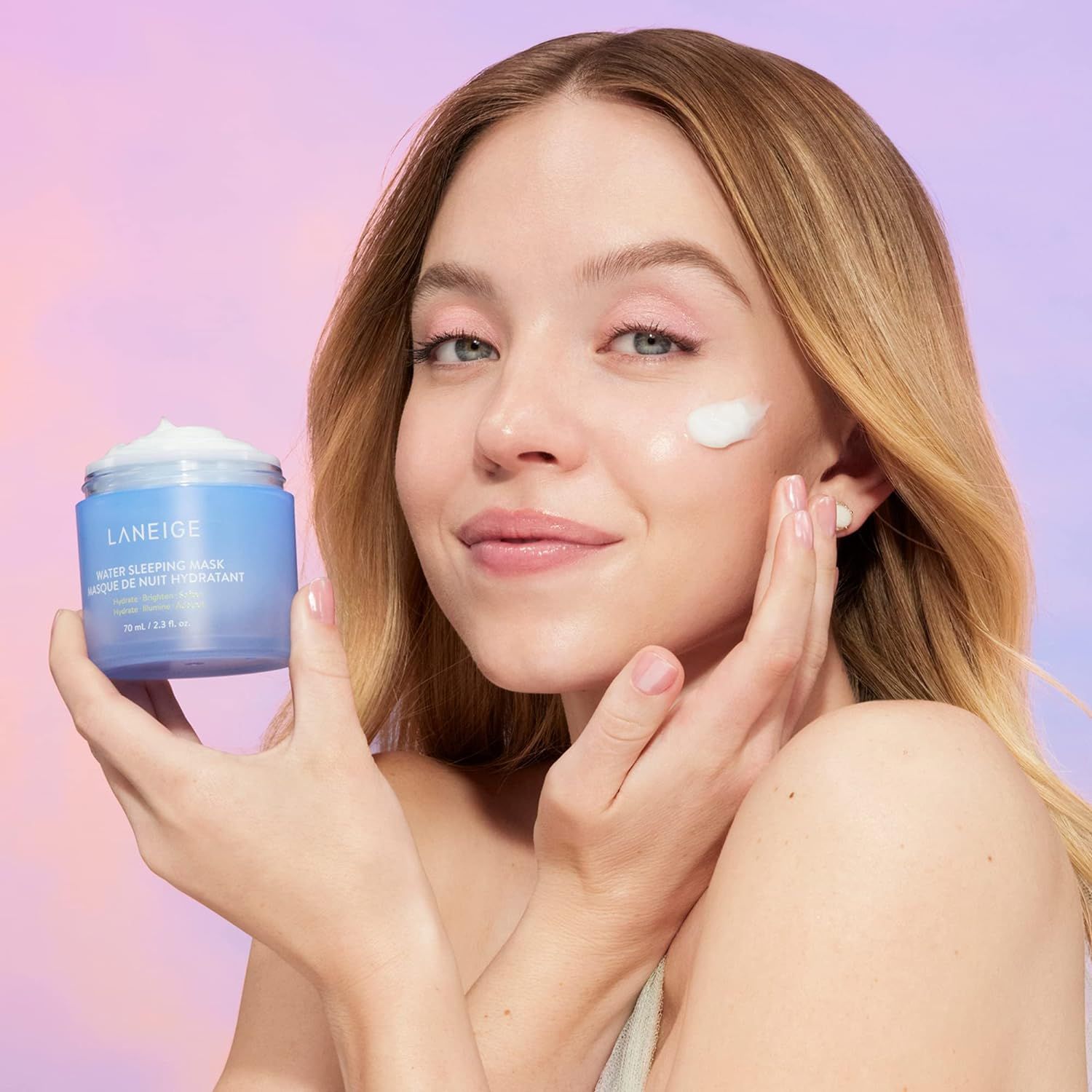 Femme tenant un pot bleu avec texte blanc: LANEIGE, WATER SLEEPING MASK. Crème sur le visage. Fond violet.