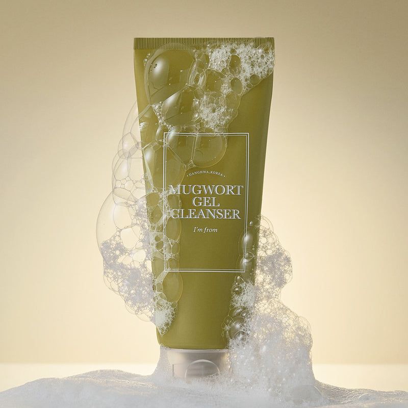 Groene tube met wit etiket, omgeven door zeepschuim. Opschrift: MUGWORT GEL CLEANSER, I'm from. Transparante sluiting.