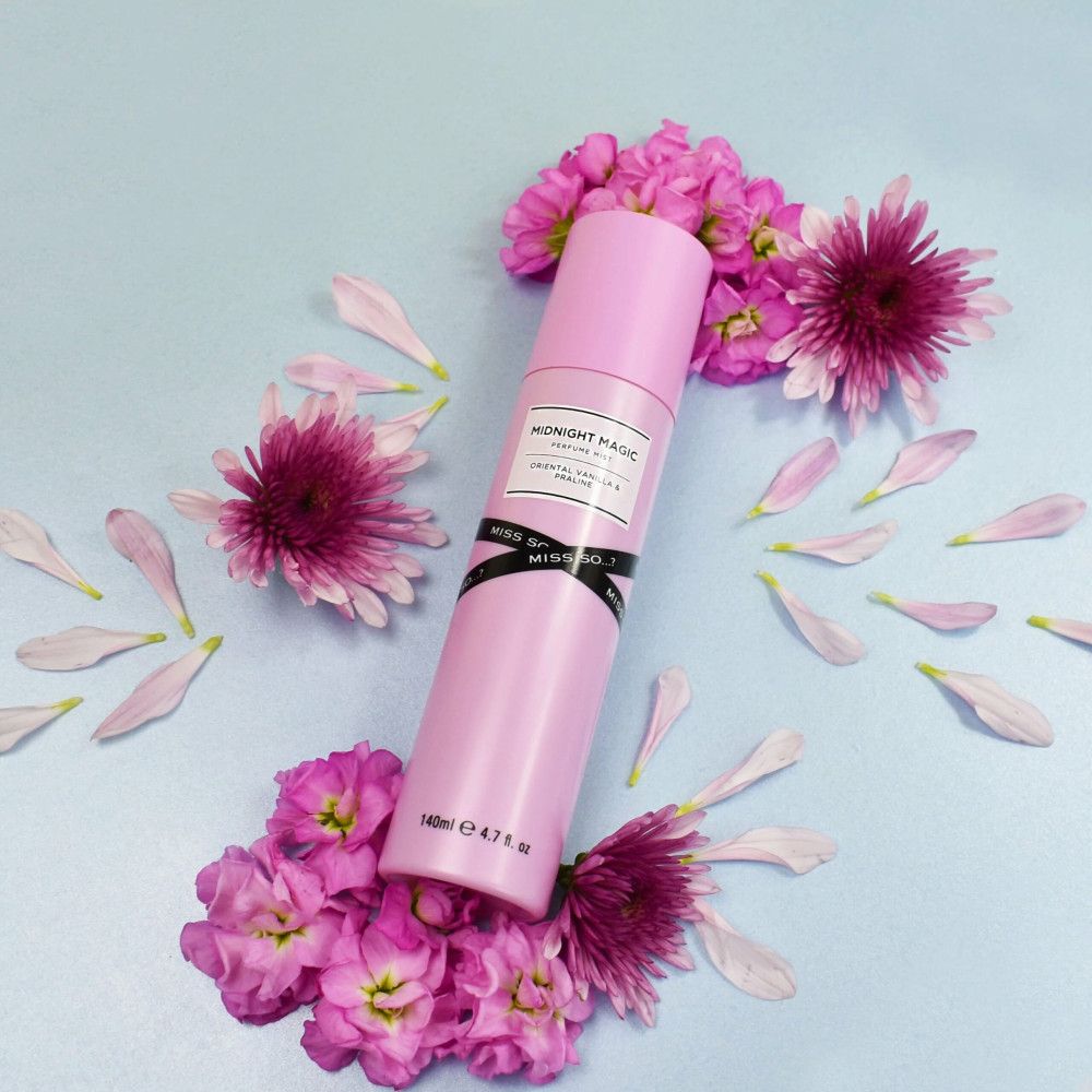 Flacon de brume corporelle rose entouré de fleurs et pétales roses. Étiquette : Midnight Magic, Oriental Vanilla & Praline. Bas : 140ml e 4.7 fl oz.