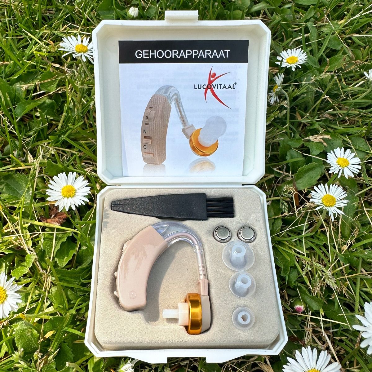 Appareil auditif dans une boîte blanche, ouvert. Comprend l'appareil, les embouts, une brosse et un manuel. Inscription : Lucovitaal.
