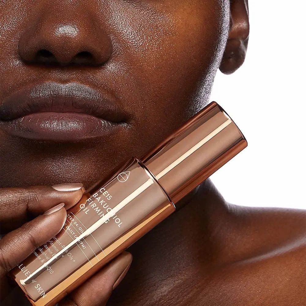 Koperkleurige oliefles met productnaam en merk. Gedeeltelijk zichtbaar: gezicht van een persoon.