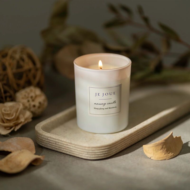 Bougie blanche allumée dans un récipient en verre. Sur un plateau. Label: Je Joue, massage candle. Arrière-plan: décoration.