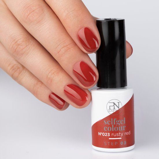 Main avec ongles vernis rouge rouille. Flacon de vernis à côté. Informations produit sur l'étiquette visibles. "N23 rusty red".