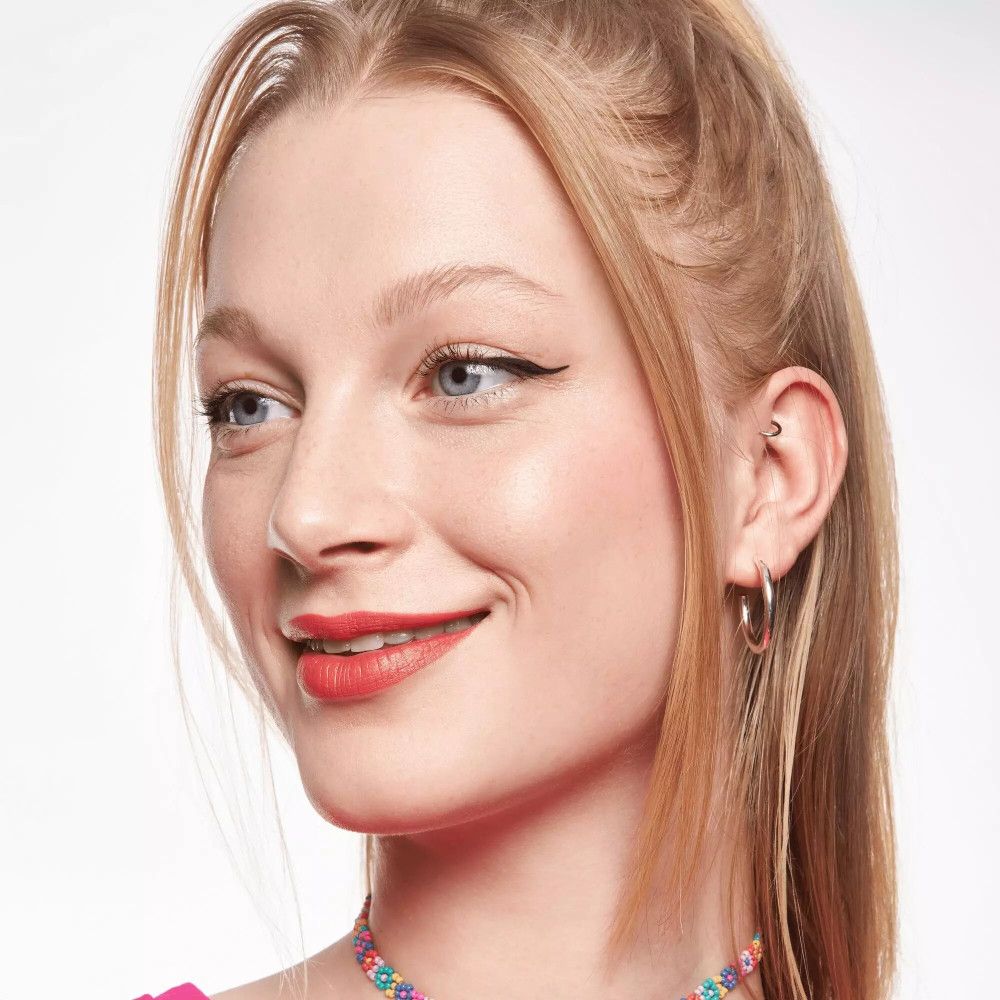 Vrouw met blond haar en roze lippenstift. Draagt oorbellen en ketting.