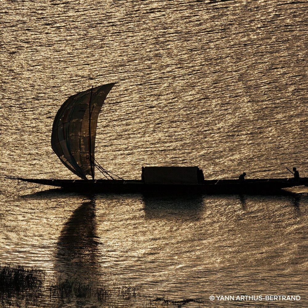 Silhouette d'un bateau à voile sur une eau scintillante. Lumière du soleil.