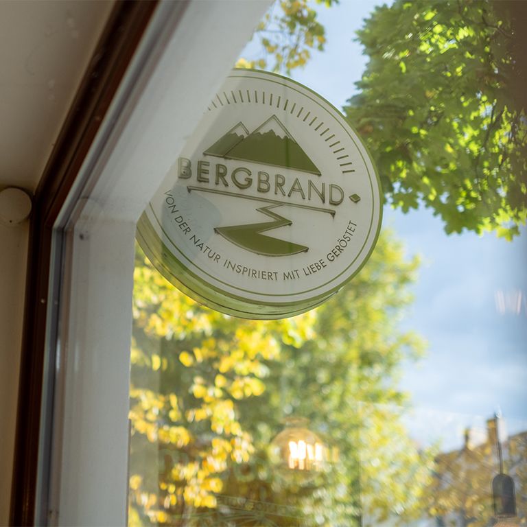 Panneau rond avec le logo BERGBRAND. Texte : Inspiré par la nature, torréfié avec amour.