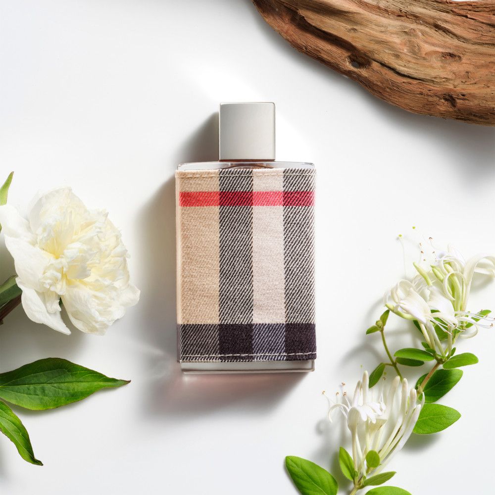 Flacon de parfum avec revêtement en tissu à carreaux. Fleurs et morceau de bois sur fond blanc.