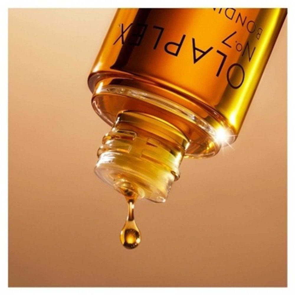 Olaplex No.7 Bonding Oil, druppels. Gouden olie druppelt uit een fles. Opschrift: Olaplex No.7 Bonding Oil.