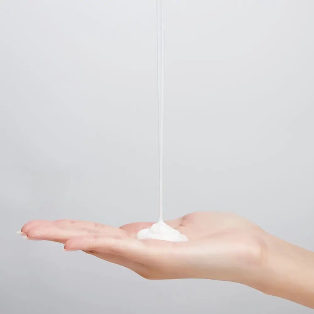 Witte crème die op een hand vloeit. Achtergrond: wit. Crèmige textuur.