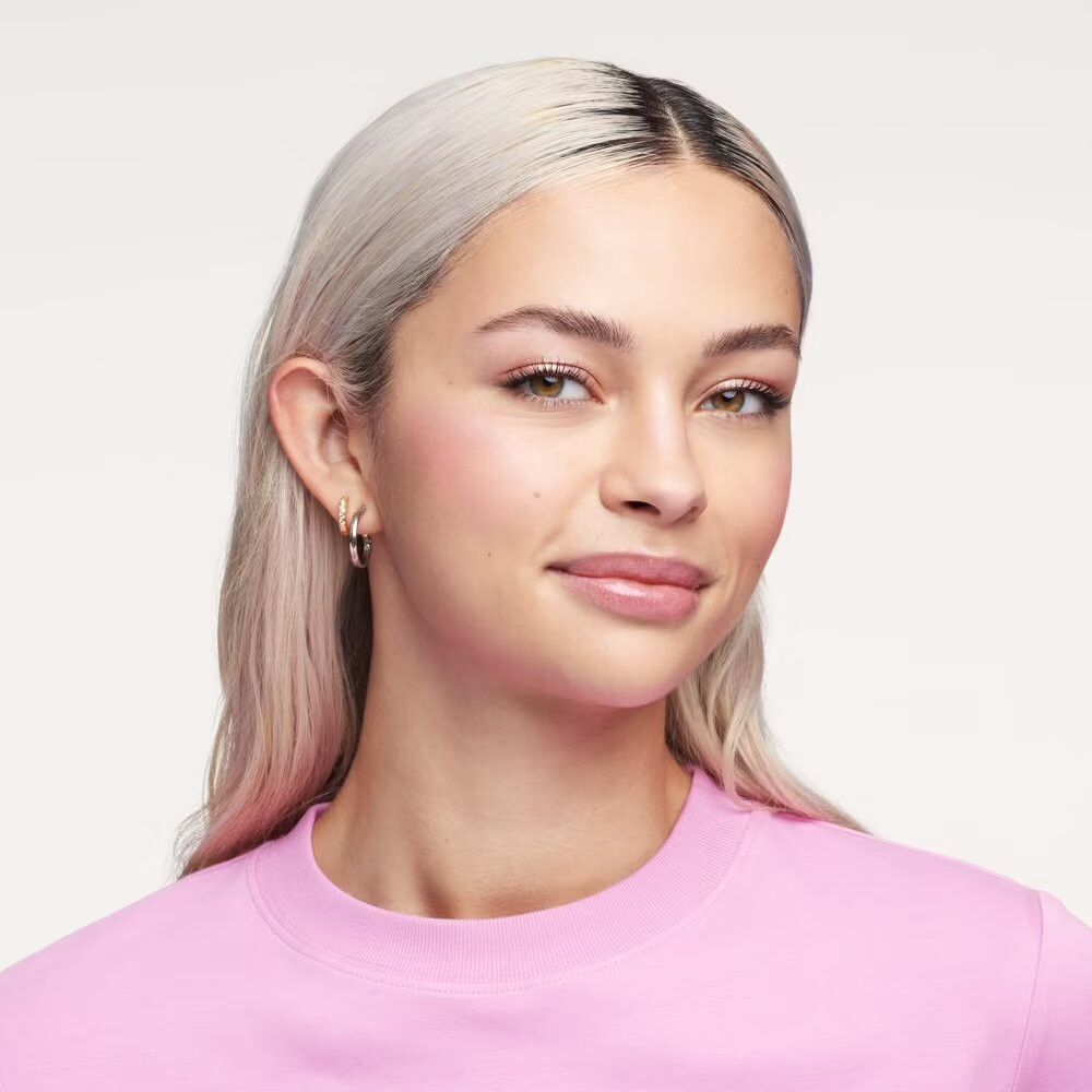 Portrait d'une femme aux cheveux blonds et sweat-shirt rose. Elle sourit. Lèvres avec gloss.