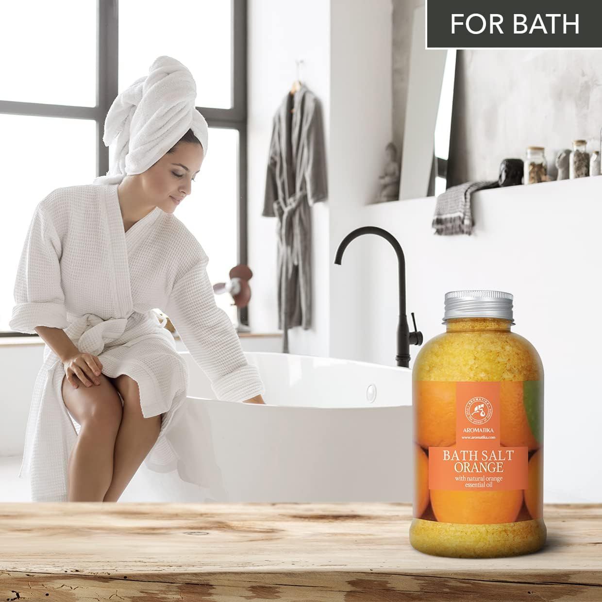 Vrouw in badjas bij de rand van het bad, naast AROMATIKA Badzout Oranje.