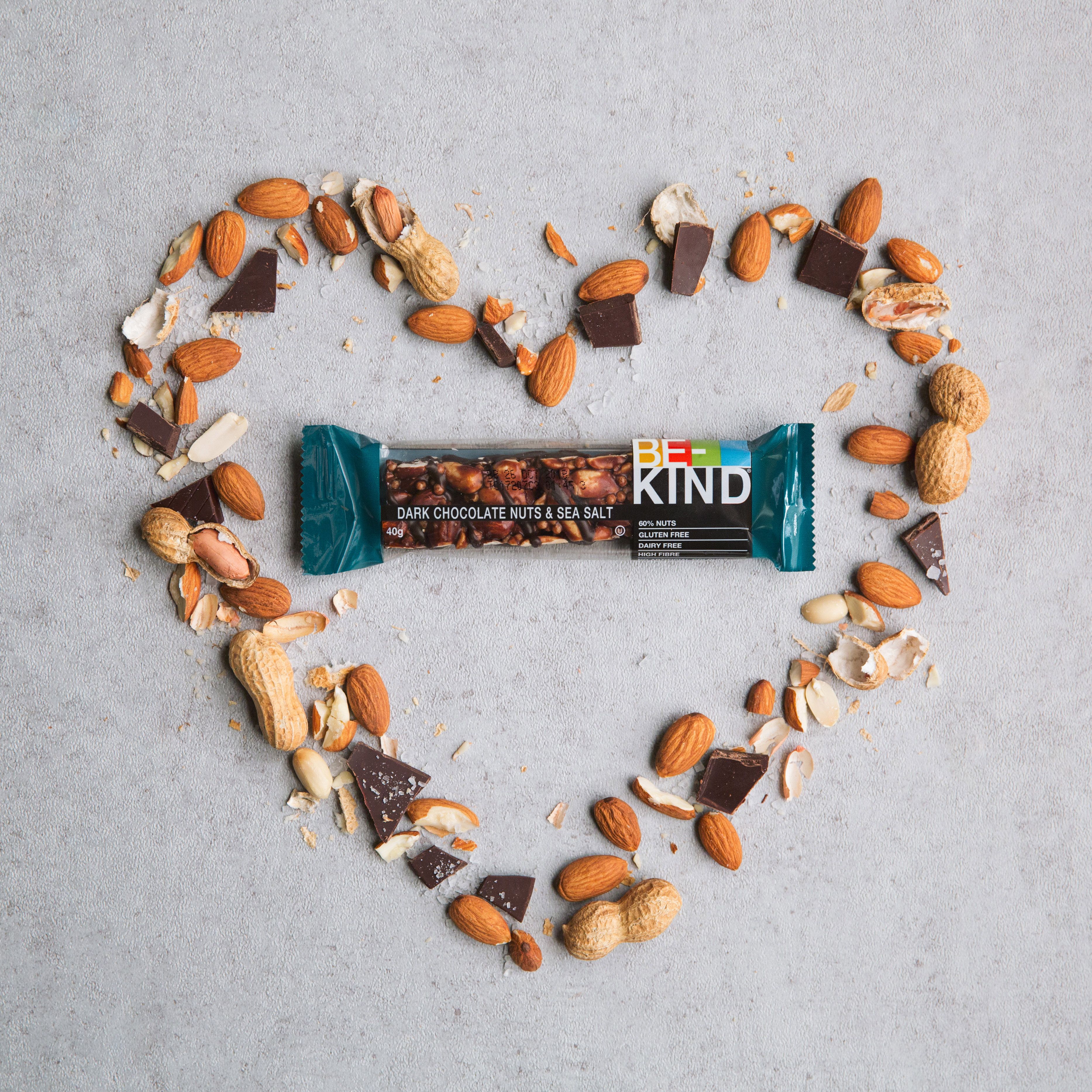Verpakte reep omringd door noten en stukjes chocolade, in hartvorm. Opschrift: BE-KIND.