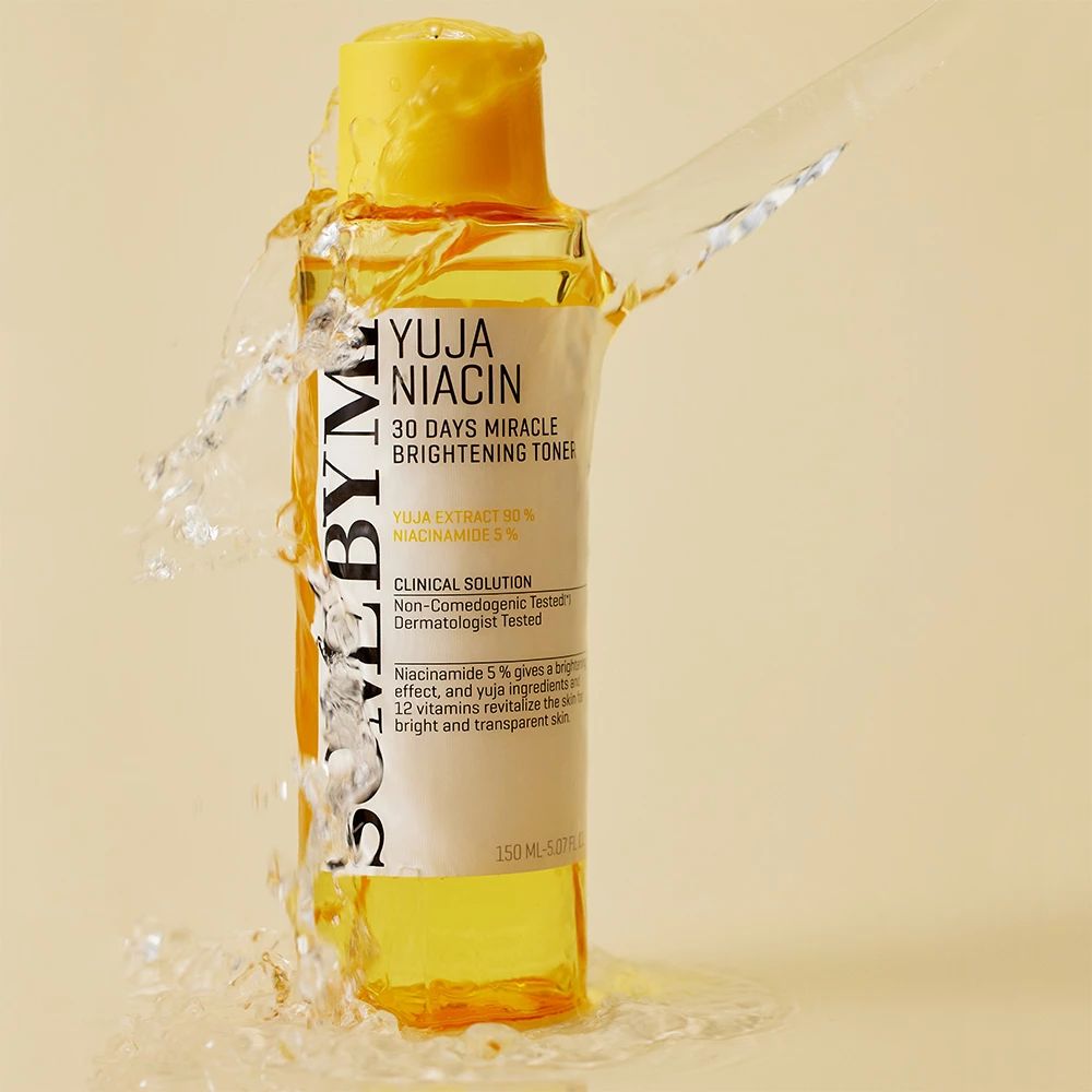 Flacon jaune avec étiquette blanche. Texte : Yuja Niacin, 30 Days Miracle Brightening Toner. De l'eau éclabousse le flacon.