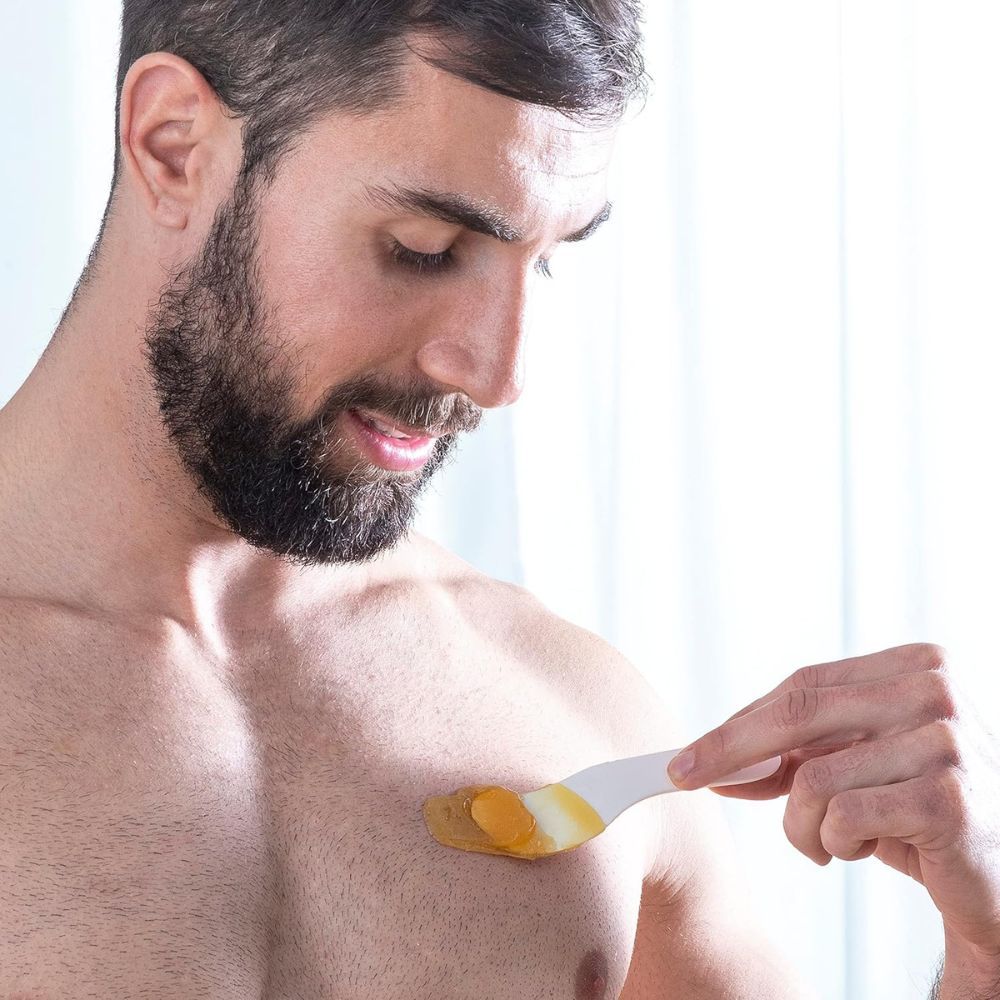 Homme appliquant de la cire sur la poitrine avec une spatule. Partie de peau visible.