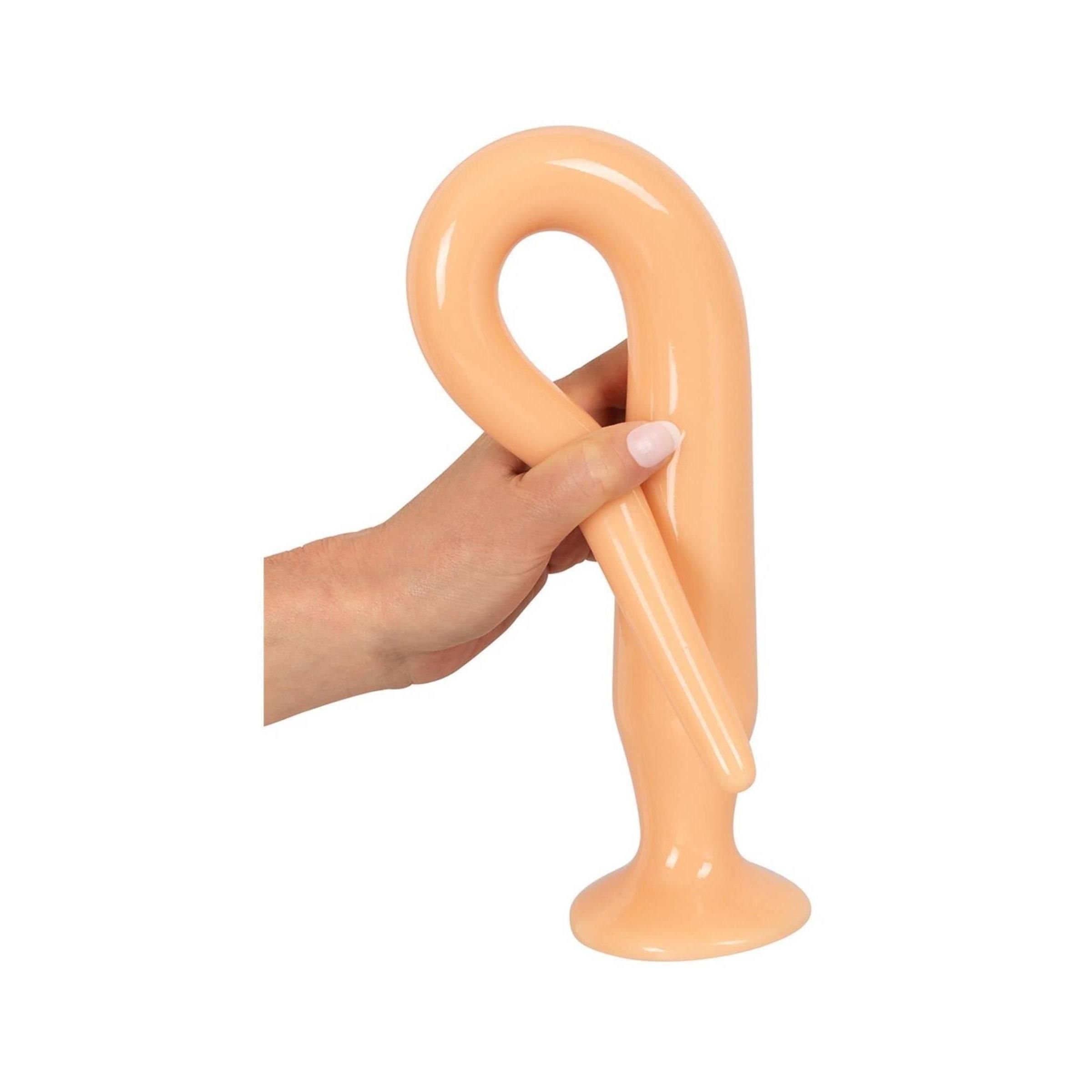 Een lichtgekleurde, flexibele anale plug, gebogen in een lus en vastgehouden in een hand.
