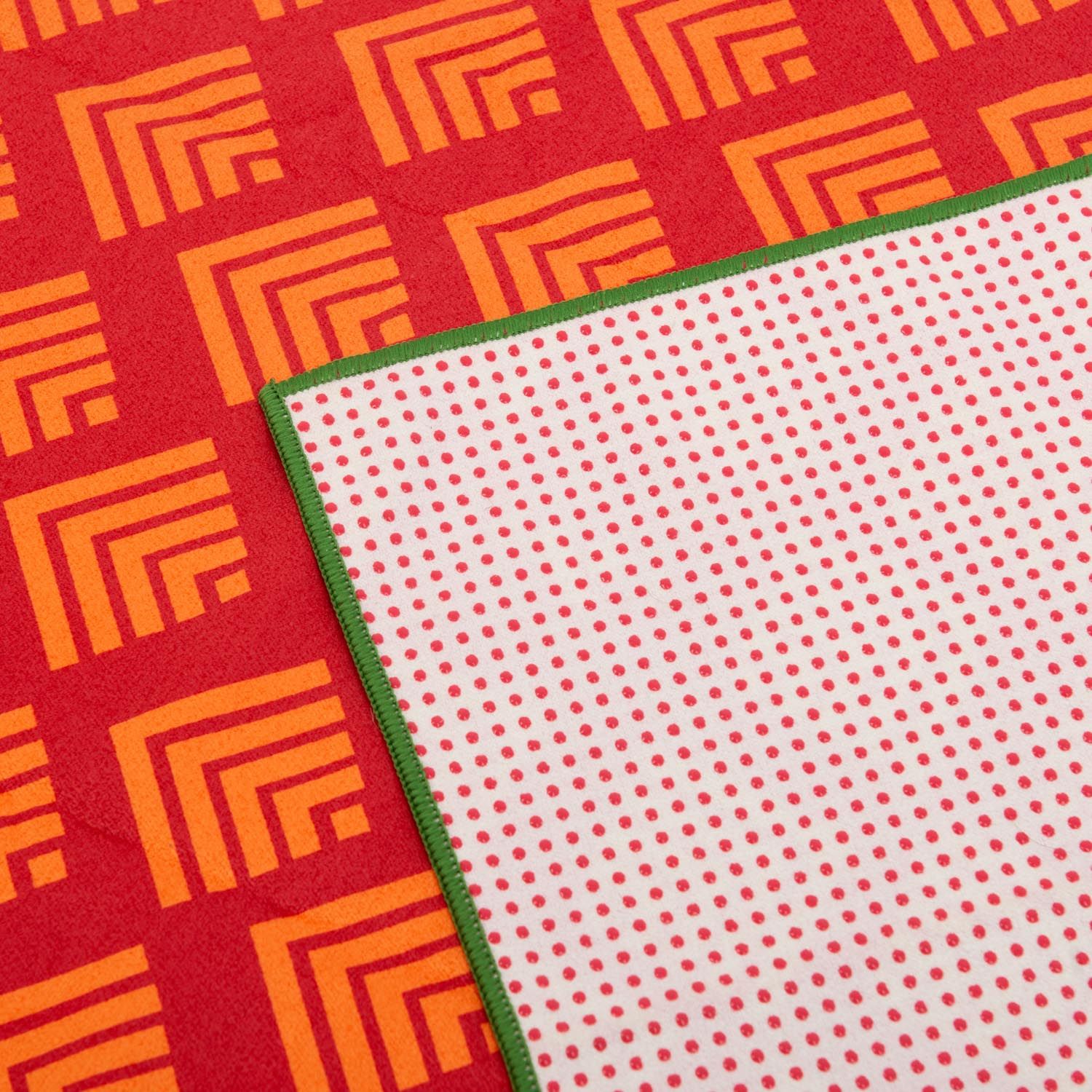 Serviette de yoga rot-gelb. Motifs géométriques, bordures vertes et dos blanc à pois rouges.