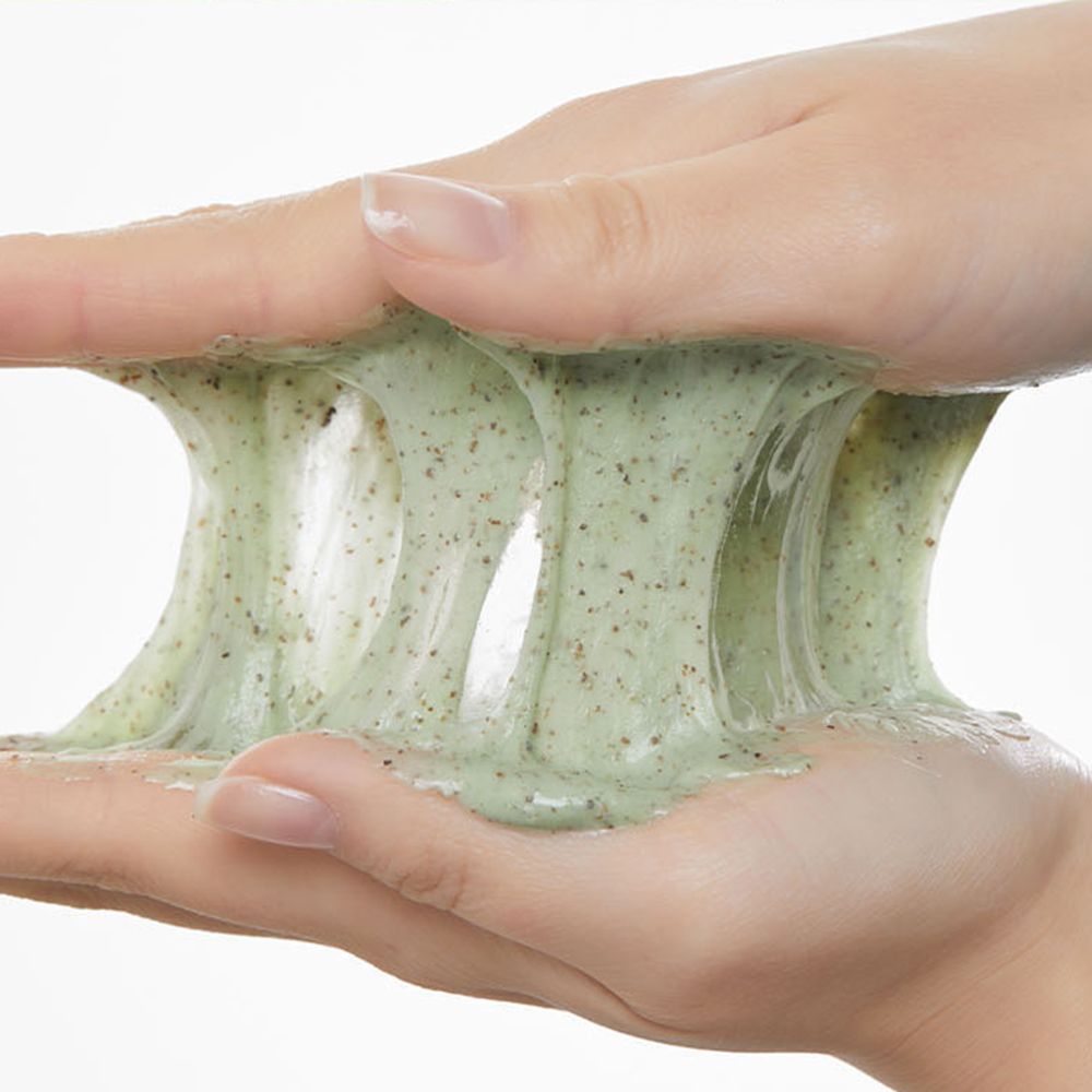 Mains tenant une substance verte gélifiée. La texture est extensible et contient de petites particules sombres.