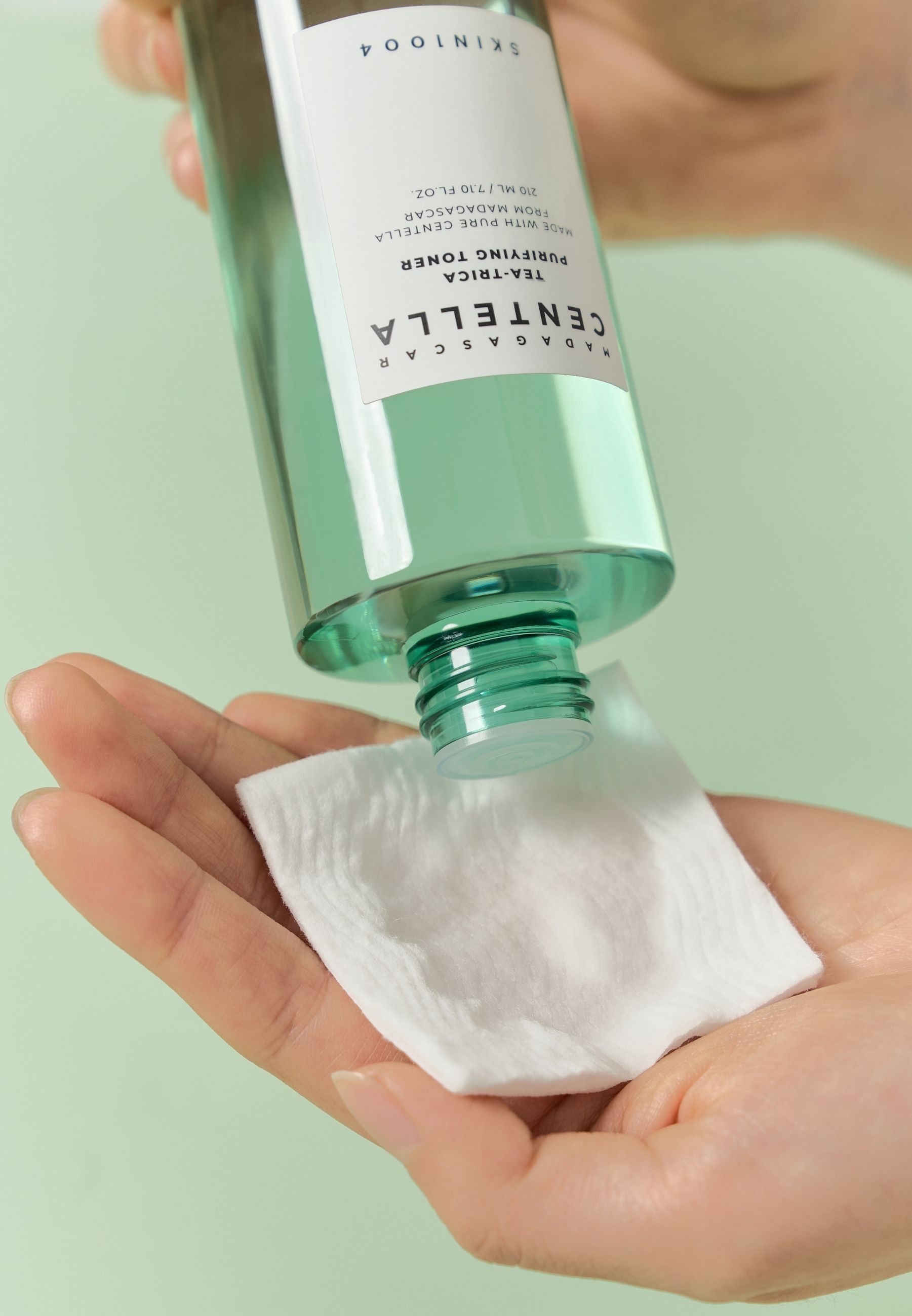 Handen houden een wattenschijfje, toner wordt uit groene fles gegoten. Label: MADAGASCAR CENTELLA.