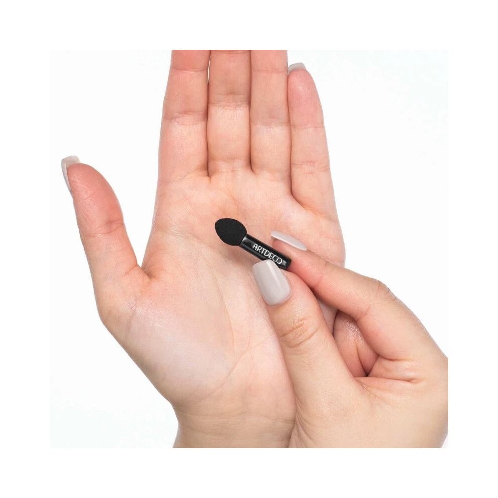 Mini applicateur d'ombres à paupières. Applicateur noir avec inscription ARTDECO. Tenu dans une main.