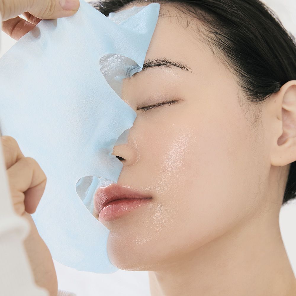 Een vrouw brengt een blauw sheetmasker aan op haar gezicht.