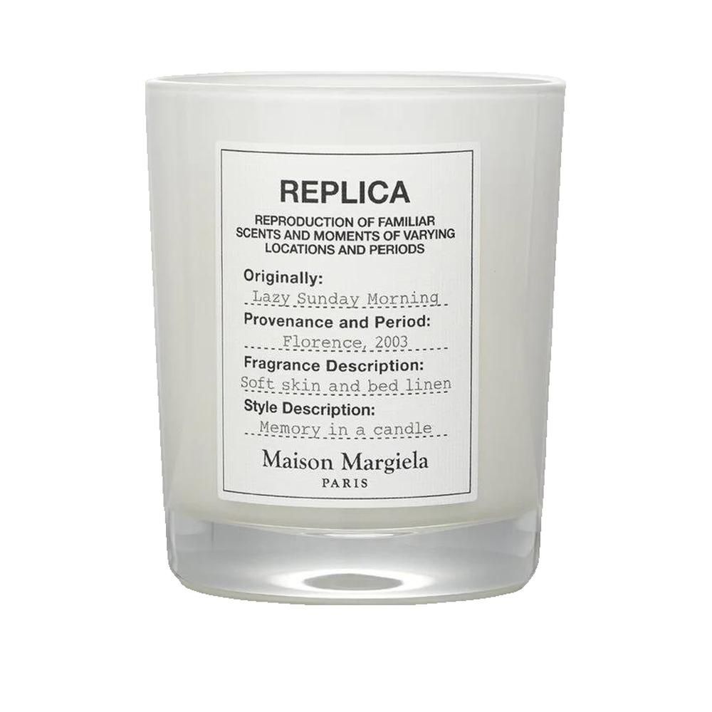 Bougie blanche avec étiquette. Texte: REPLICA, Maison Margiela. Description du produit sur l'étiquette.