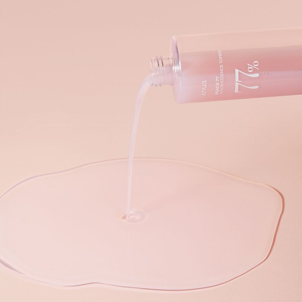 Le toner essence niacine ANUA Peach 77% est versé d'une bouteille sur une surface.
