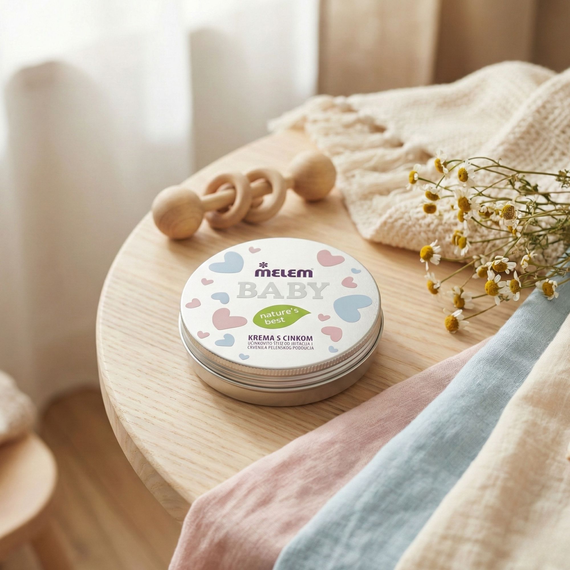 Boîte ronde Melem Baby sur une table avec un hochet en bois et des couches. Fleurs de camomille.