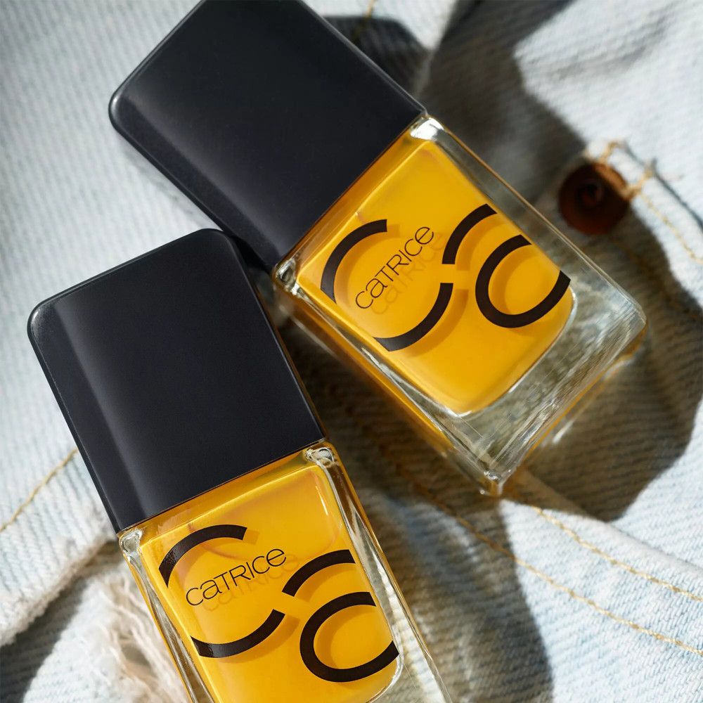 Deux flacons de vernis à ongles Catrice avec bouchon noir et contenu jaune. Logo Catrice sur les flacons, sur tissu jean.