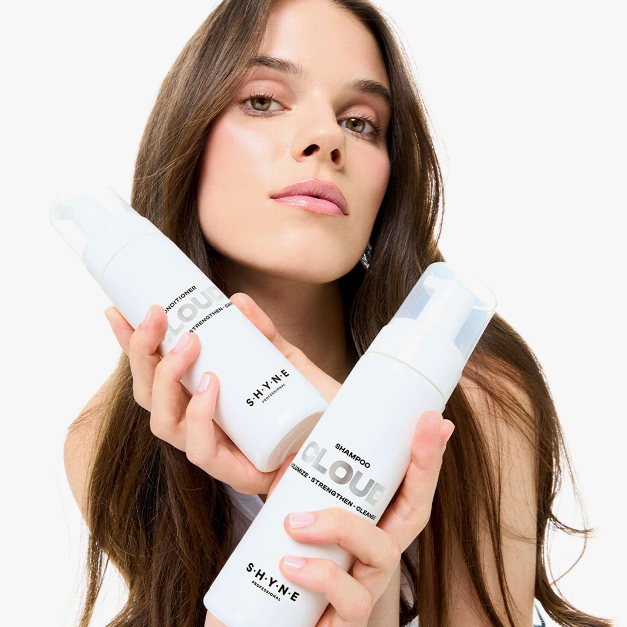 Vrouw houdt twee witte flessen vast: SHYNE Cloud Conditioner en Shampoo. Met pomp.