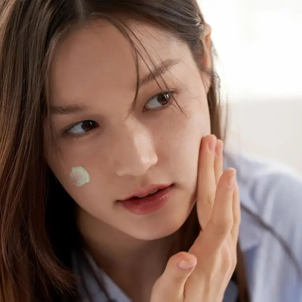 Vrouw brengt groene make-up primer aan op haar gezicht.