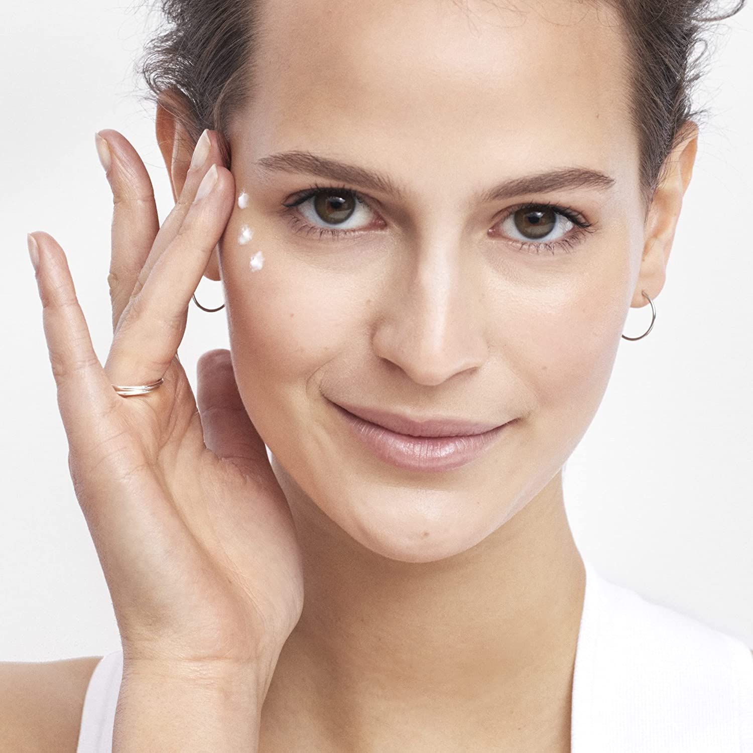 Femme appliquant de la crème. Peau claire, vêtements clairs. Points de crème sous les yeux.