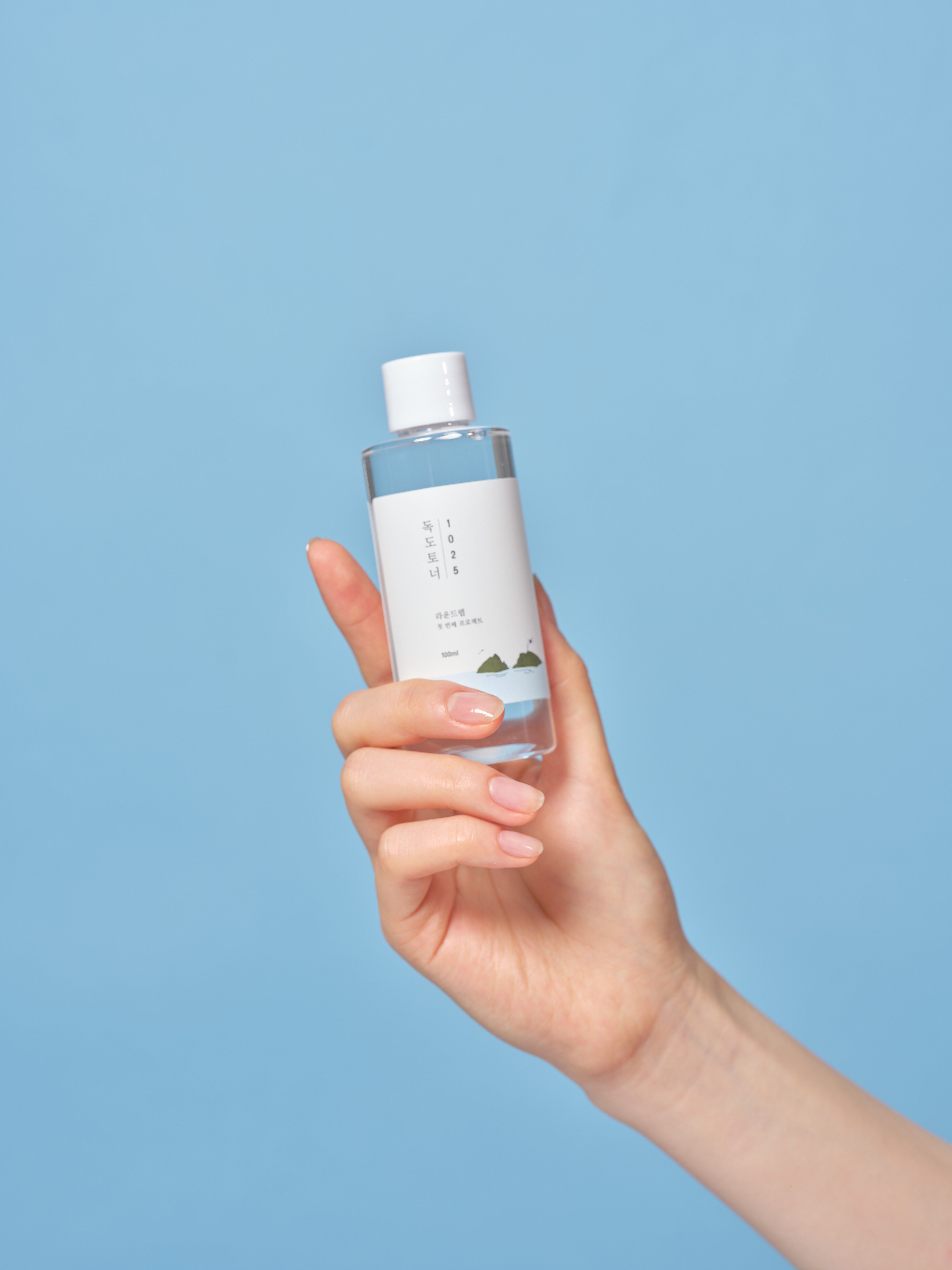 Hand die een transparante fles met witte dop vasthoudt. Het etiket bevat Koreaanse tekst.