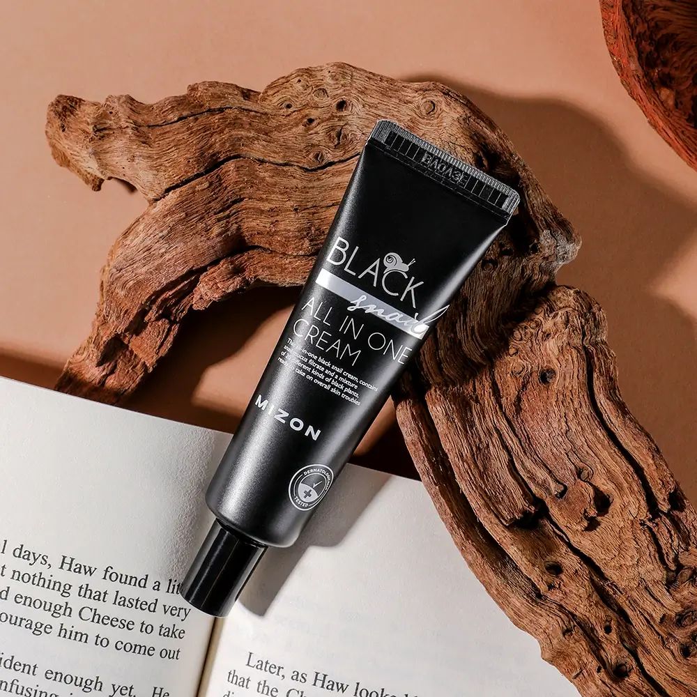 Zwarte tube met opschrift BLACK snail ALL IN ONE CREAM en MIZON. Op hout en boek.